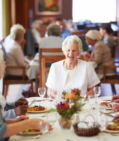 Alte Frau lacht am Tisch sitzend