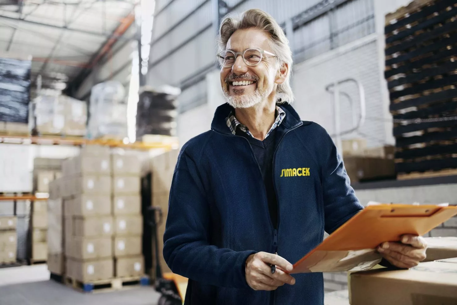 Mann mit blauer Simacek-Jacke steht in großem Lagergebäude