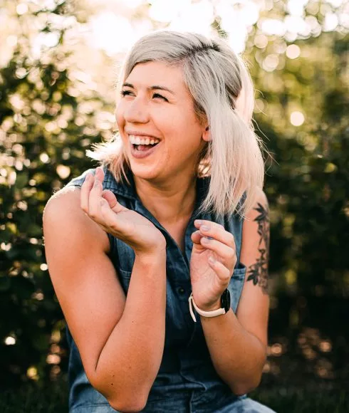 lachende blonde Frau vor einer Hecke